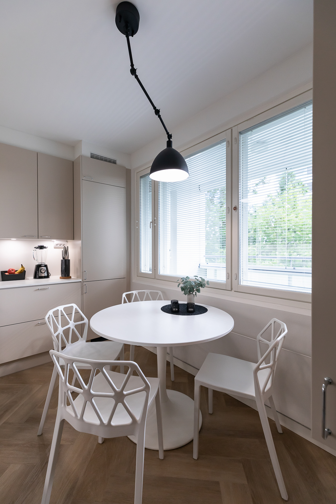 Ruokapöytä ikkunan äärellä, moderni valaistus ja harmoninen sisustussuunnittelu Oulussa.